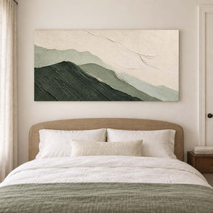 Layered dark and pale green mountains beneath an ivory sky without an outer frame, displayed above a bed.