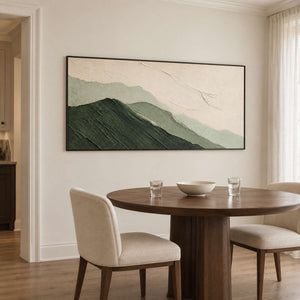 Layered dark and pale green mountains beneath an ivory sky in a black frame, displayed above a dining table.
