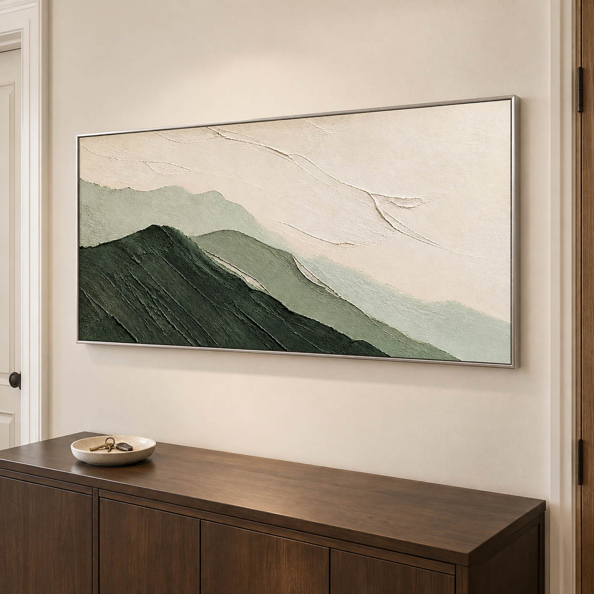 Layered dark and pale green mountains beneath an ivory sky in a silver frame, displayed above an entryway console.