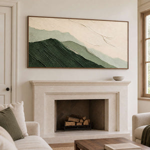 Layered dark and pale green mountains beneath an ivory sky in a brown wood frame, displayed above a fireplace.