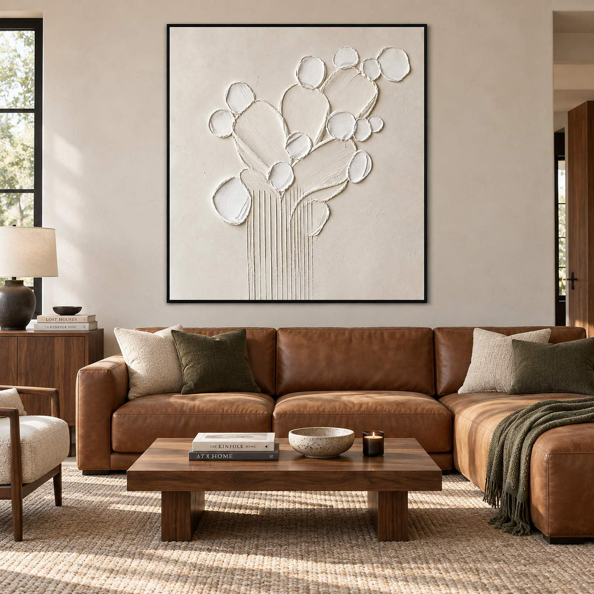 Sculptural warm white petals and leaves raised from a monochrome canvas, displayed in a living room in a black frame.