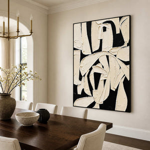Black framed abstract artwork with sweeping ivory gestures above a wooden dining table.
