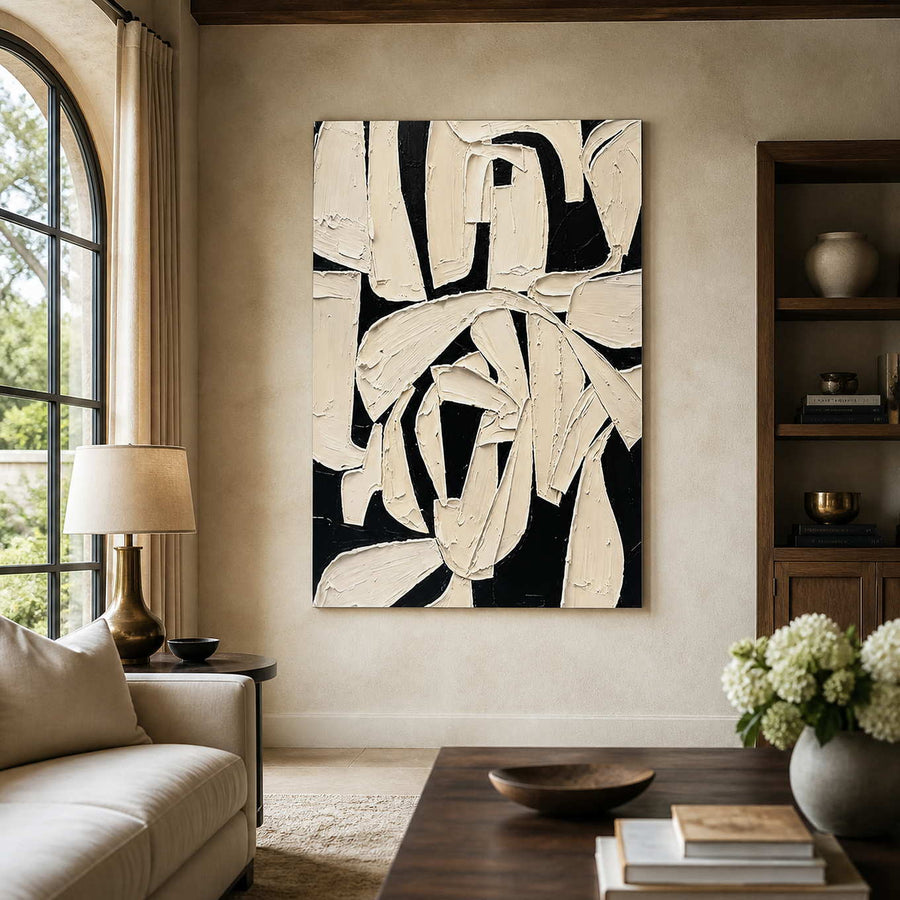 Frameless ivory and black abstract artwork with overlapping strokes beside a living room sofa.