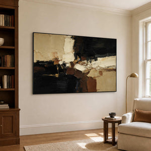 Black framed earthy abstract artwork beside wooden bookshelves and a cream reading chair.