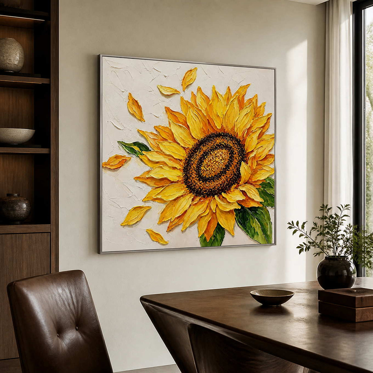Silver-framed sunflower painting beside a dark wooden desk and a brown leather chair in a sunlit study.
