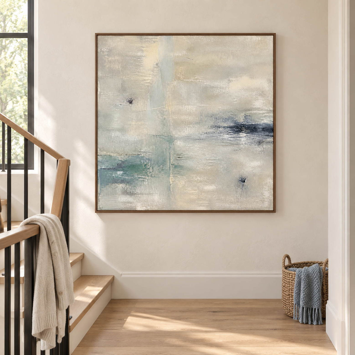 Square neutral abstract painting with ivory, pale aqua, and blue-gray marks in a brown wood frame on a stair landing.