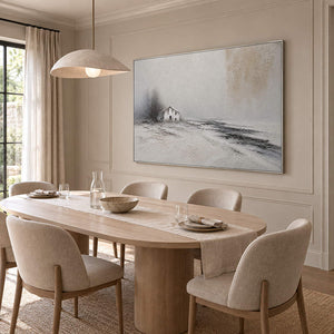 Winter landscape painting with a small house and dark trees beyond a snowy field in a silver frame in a dining room.