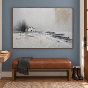 Winter landscape painting with a small house and dark trees beyond a snowy field in a brown wood frame in an entryway.