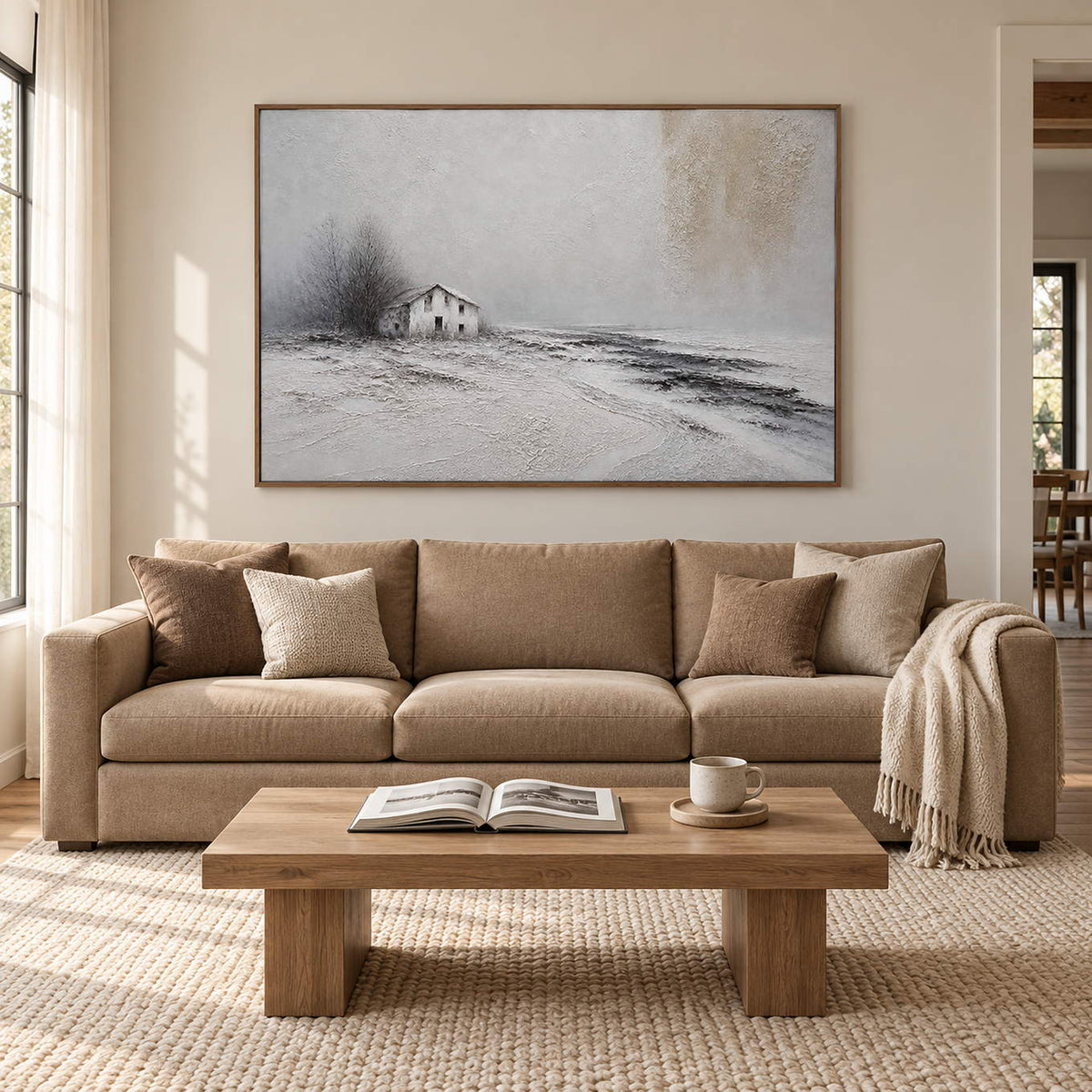 Winter landscape painting with a small house and dark trees beyond a snowy field in a brown wood frame in a living room.