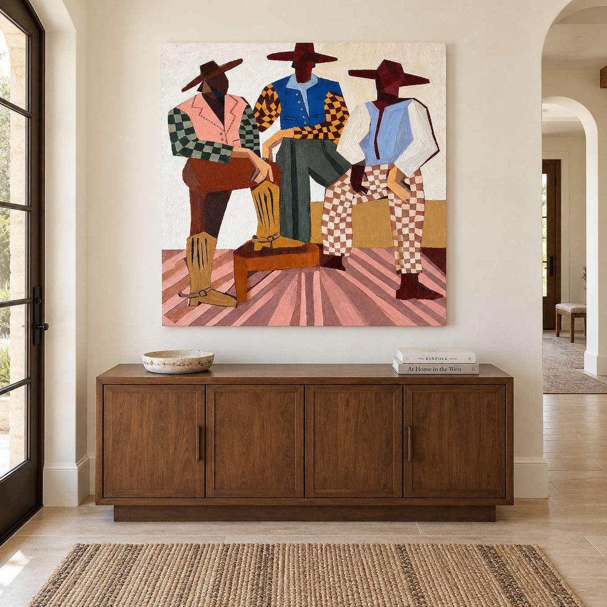 Square three-figure painting above a paneled wood cabinet near a tall window.