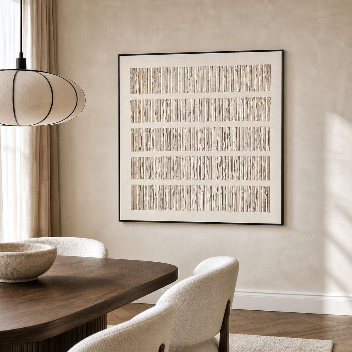 Black framed pale textured artwork above a wooden dining table with cream chairs.
