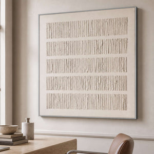 Silver framed ridged abstract artwork beside a wooden desk and leather chair.