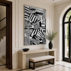 Silver-framed abstract wall art above a stone console beside an arched entryway window.