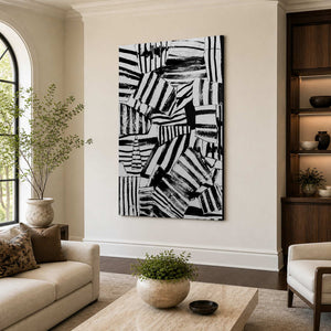 Frameless black and white abstract wall art between neutral seats in a bright living room.