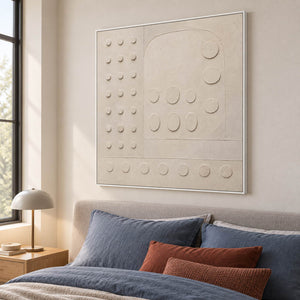 Warm white textured wall art with raised circles and quiet geometry, displayed in a bedroom in a white frame.