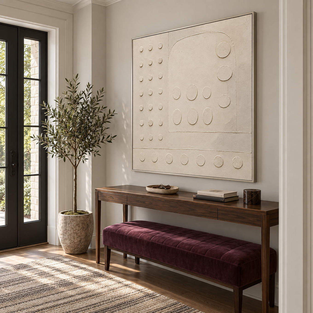 Warm white textured wall art with raised circles and quiet geometry, displayed in an entrance hall in a silver frame.