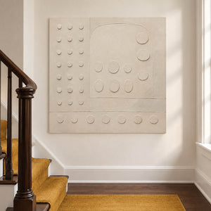 Warm white textured wall art with raised circles and quiet geometry, displayed beside a staircase without an outer frame.