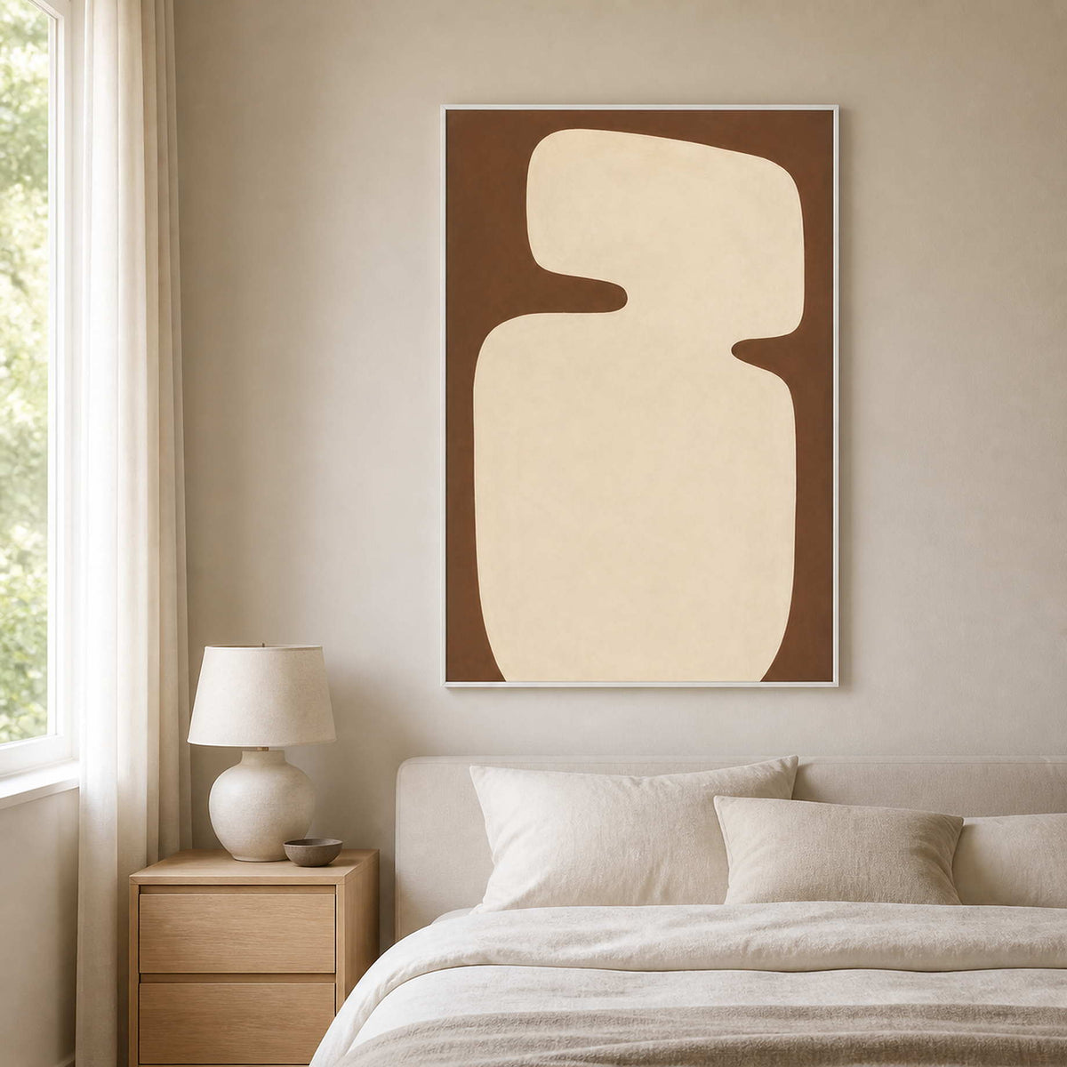 White framed cream and brown painting above a padded headboard in a quiet bedroom.