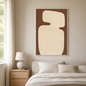 White framed cream and brown painting above a padded headboard in a quiet bedroom.