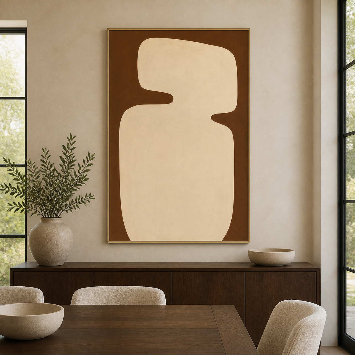 Gold framed cream organic shape above a wood sideboard in a bright dining room.