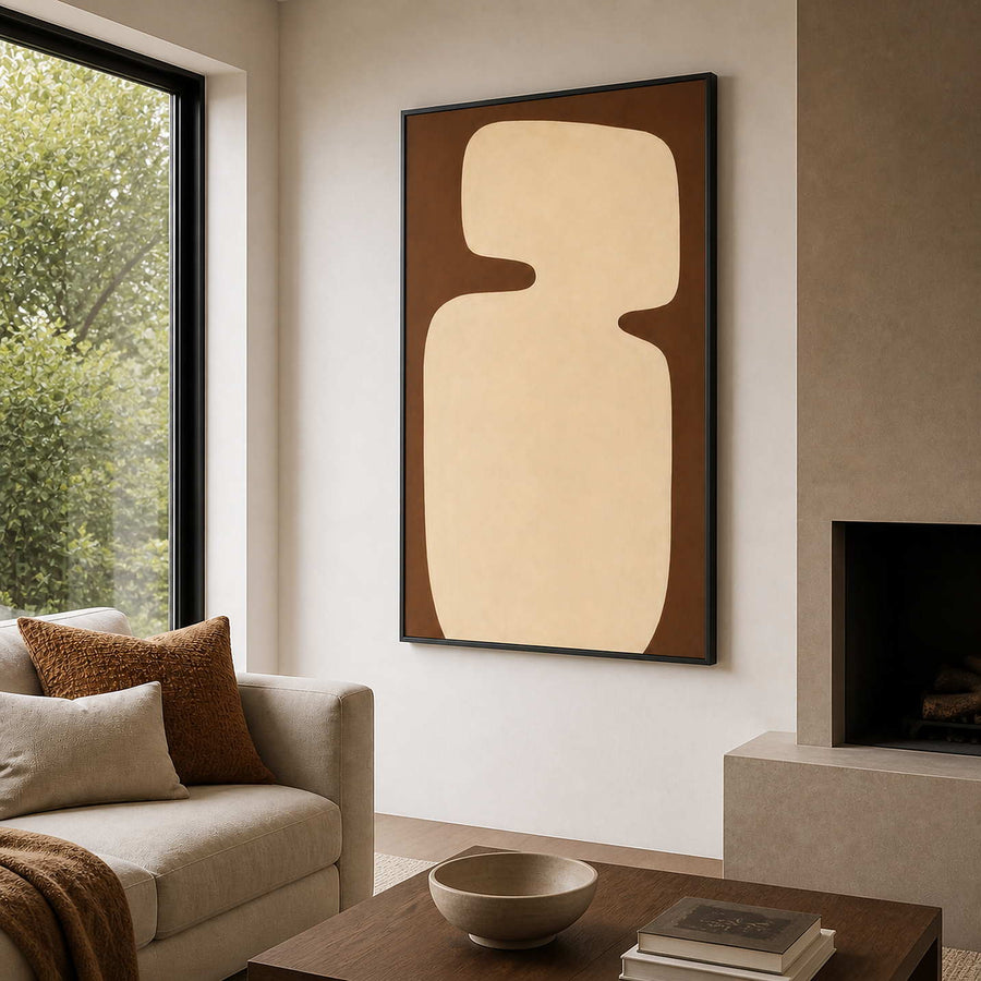 Black framed cream and brown abstract painting beside a sofa and living room fireplace.
