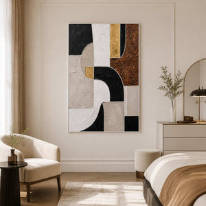 White framed geometric artwork beside a bed and cream chair in a bright bedroom.