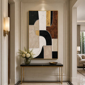 Gold framed geometric artwork above a dark console with white flowers in a hallway.