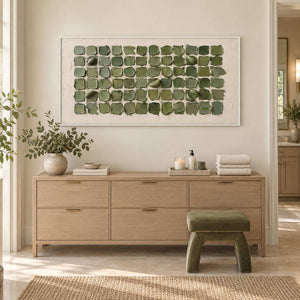 Keeping a Little Spring in a white frame above a light wood cabinet with folded towels and a green stool nearby.