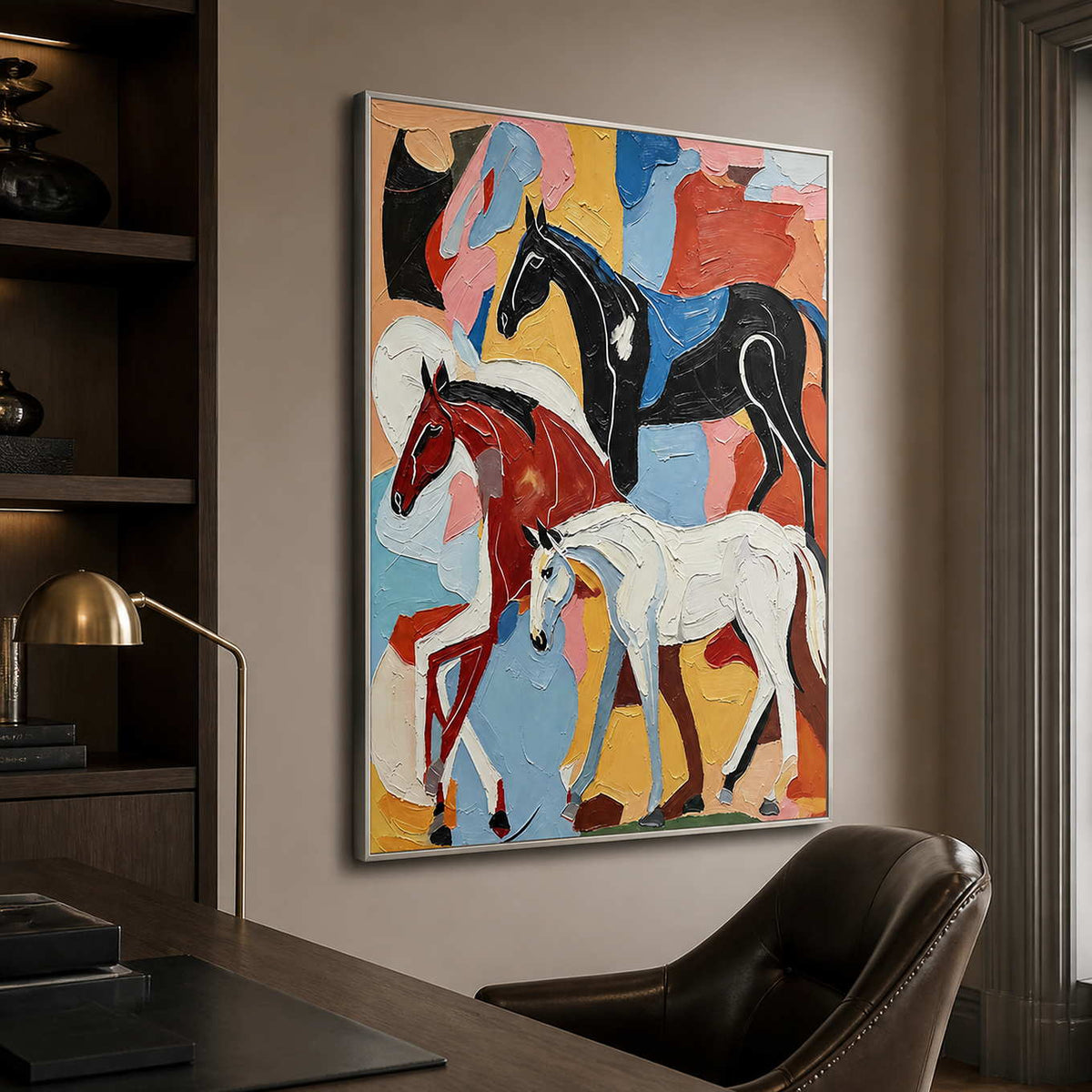 Silver framed artwork showing three colorful horses beside a home office bookshelf.