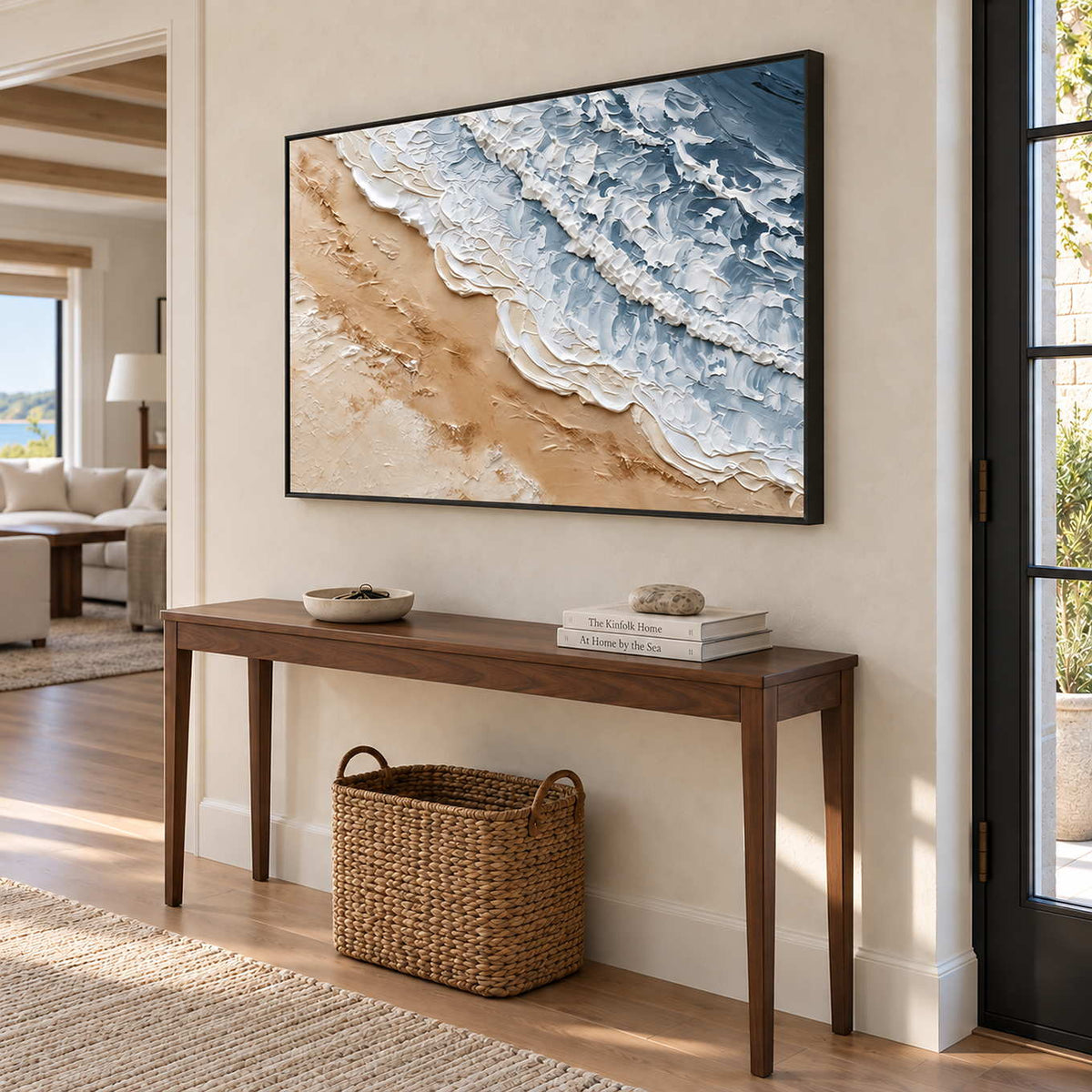 Kissing the Shore in a black frame above a wood entryway console with a woven basket beneath.