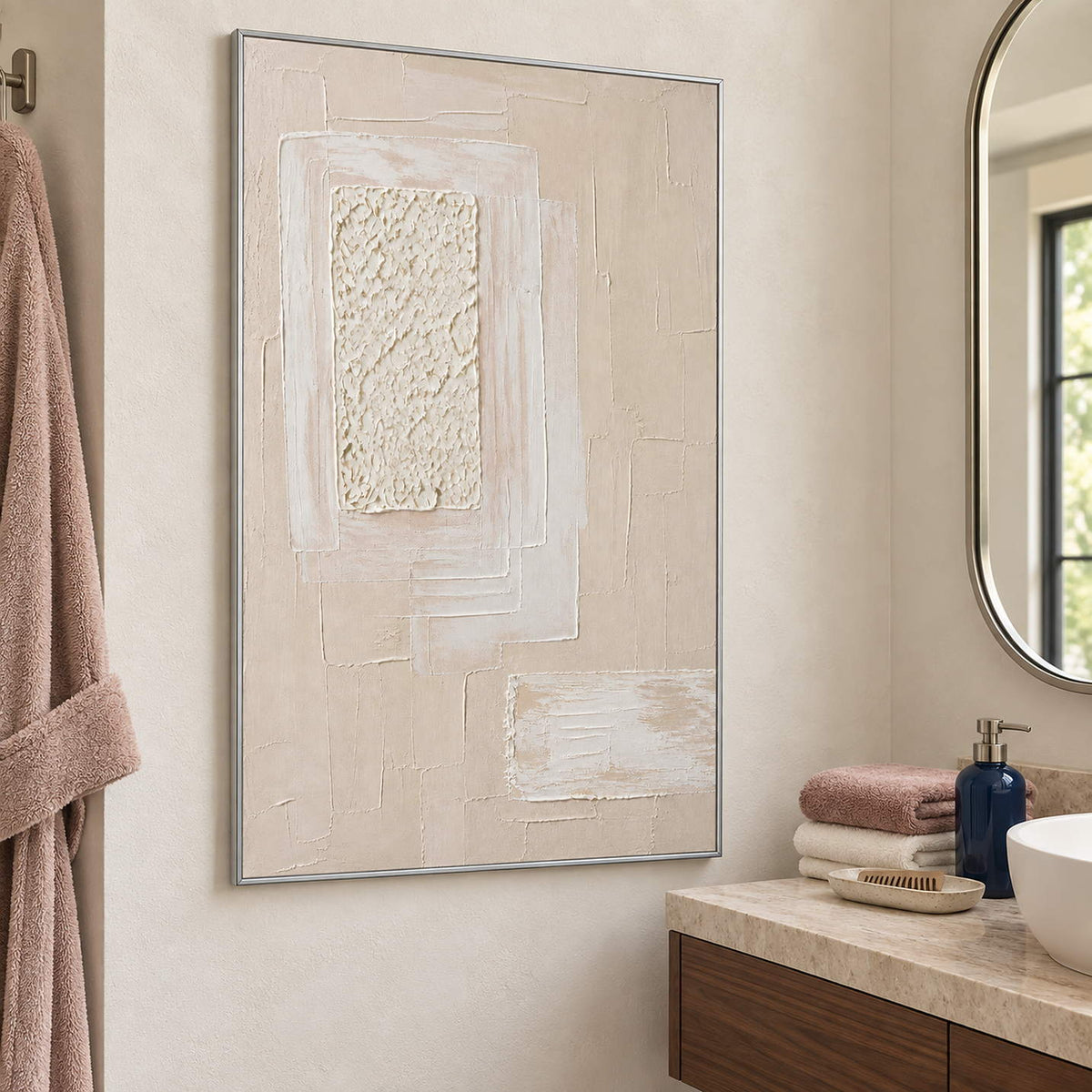Ivory and blush relief painting with layered rectangles and a rough central panel in a silver frame beside a bathroom vanity.