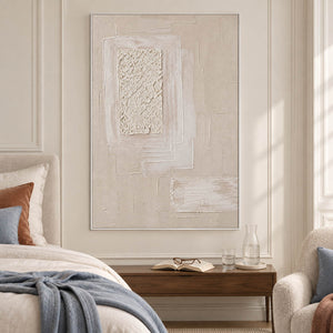 Ivory and blush relief painting with layered rectangles and a rough central panel in a white frame in a bedroom.