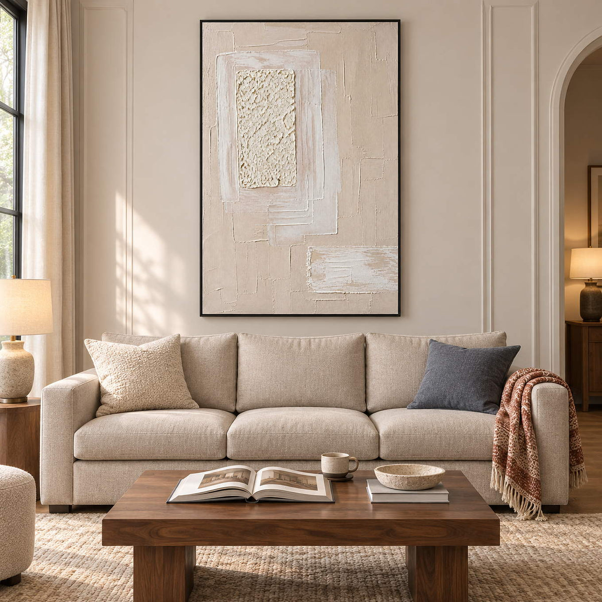 Ivory and blush relief painting with layered rectangles and a rough central panel in a black frame in a living room.