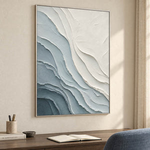 Layered blue-gray and chalk-white coastal relief painting in a silver frame in a home office.