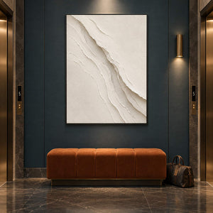 Hand-painted ivory abstract wall art with layered cream palette-knife relief, displayed in a hotel elevator lobby in a black frame.