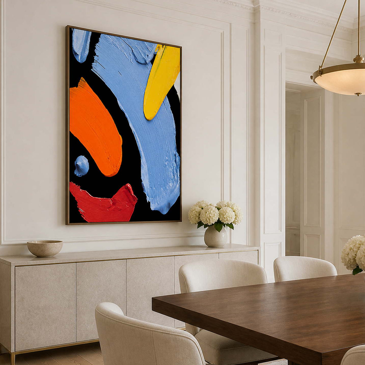 Wood framed colorful abstract painting above a pale sideboard beside a wooden dining table.