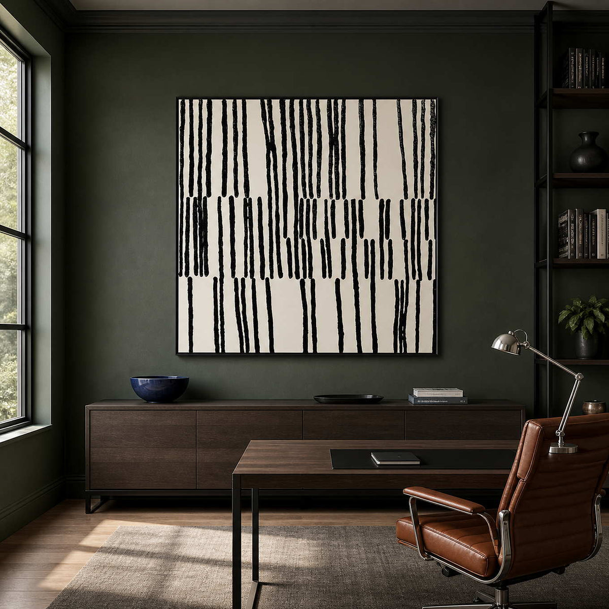Black framed patterned artwork beside a wooden desk against a dark green wall.