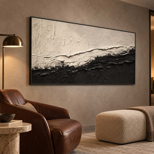 Monochrome textured painting beside a brown reading chair and cream ottoman.