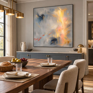 Blue-gray abstract painting with gold, blush, and dark blue marks in a black frame in a dining room.