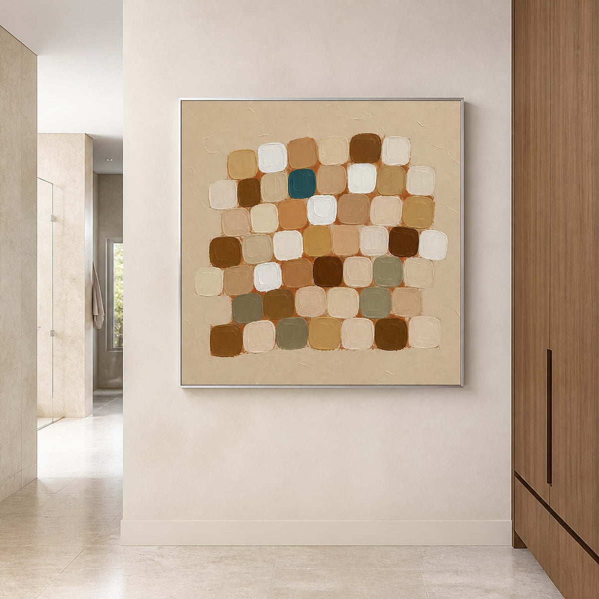 Silver framed neutral square painting beside pale stone shower walls and wooden cabinets.