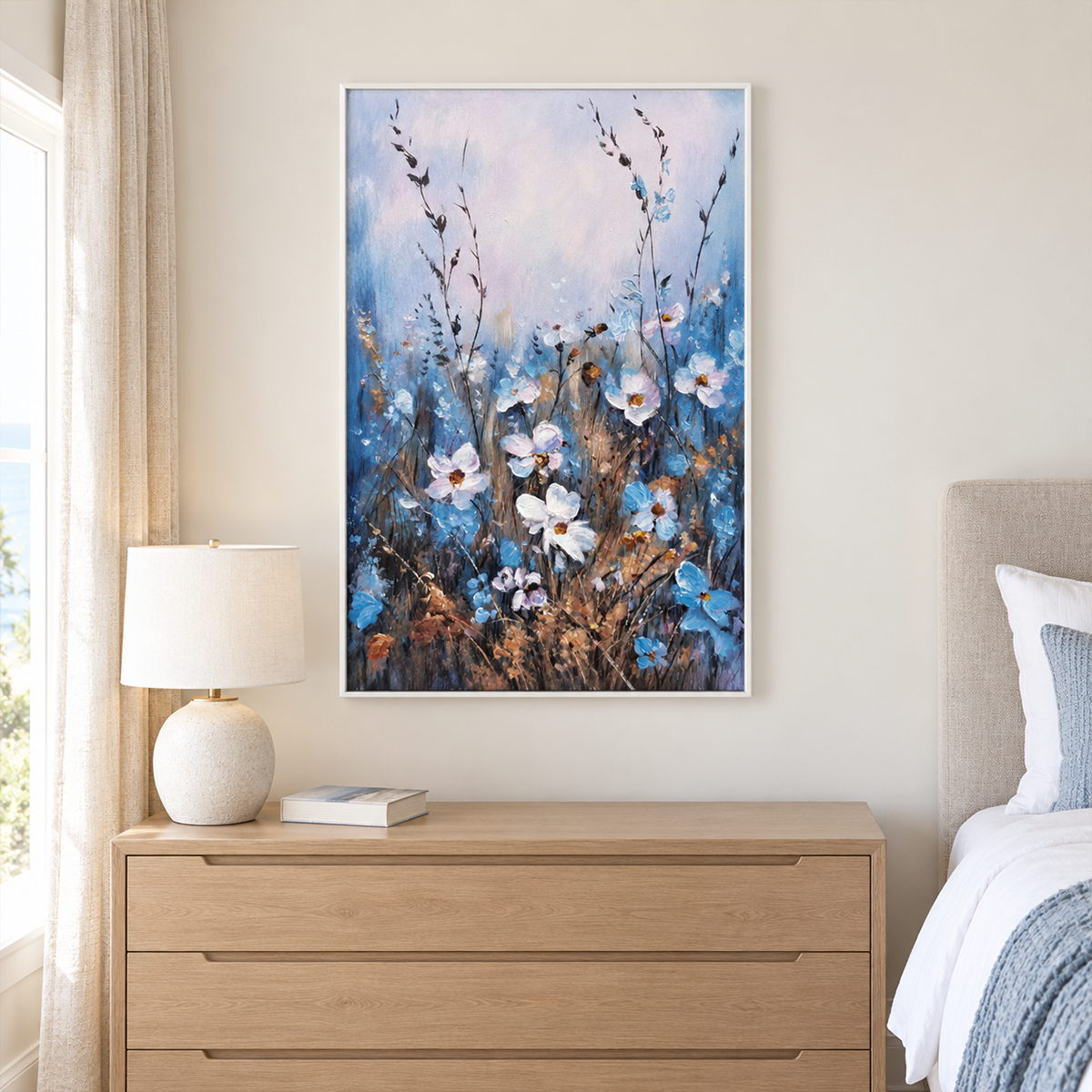In a bedroom near the bed, an artwork with a white frame shows white and blue wildflowers on slender stems beneath a broad pale upper area.