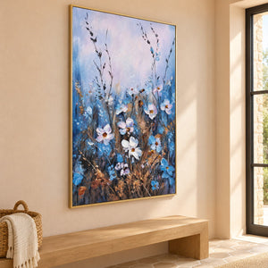 Artwork showing white and blue wildflowers on slender stems beneath a broad pale upper area in a hallway above a bench, with a gold-colored frame.