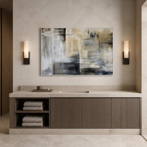 White framed gray and beige painting above a stone vanity between bathroom sconces.