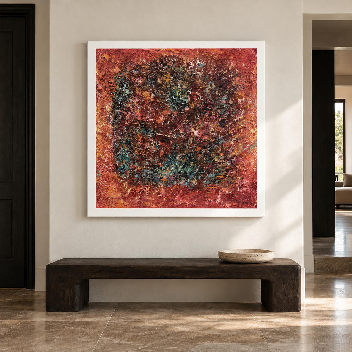 A dark textured ring surrounded by rust red and orange with scattered turquoise flecks in an artwork with no outer frame, displayed in an entryway above a console or bench.