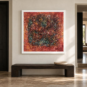 A dark textured ring surrounded by rust red and orange with scattered turquoise flecks in an artwork with no outer frame, displayed in an entryway above a console or bench.
