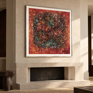 A dark textured ring surrounded by rust red and orange with scattered turquoise flecks in an artwork with a silver-colored frame, displayed above a fireplace.