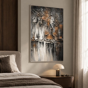 In a bedroom near the bed, an artwork with a white frame shows dark gray and brown flaking forms above horizontal strata and pale vertical streaks.
