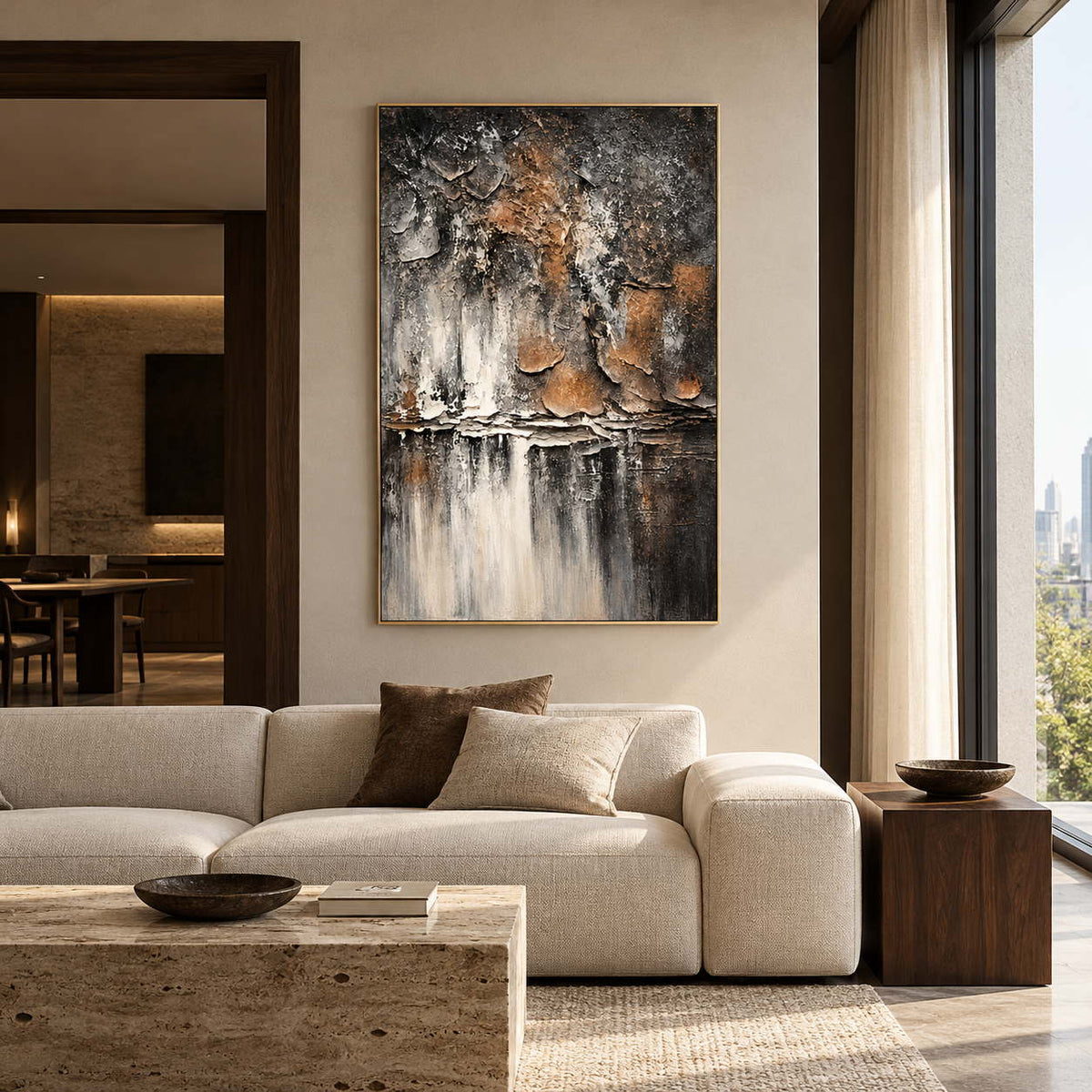Dark gray and brown flaking forms above horizontal strata and pale vertical streaks in an artwork with a gold-colored frame, displayed in a living room above seating.