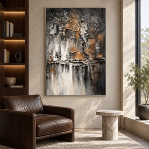 Artwork showing dark gray and brown flaking forms above horizontal strata and pale vertical streaks beside a reading chair, with a silver-colored frame.