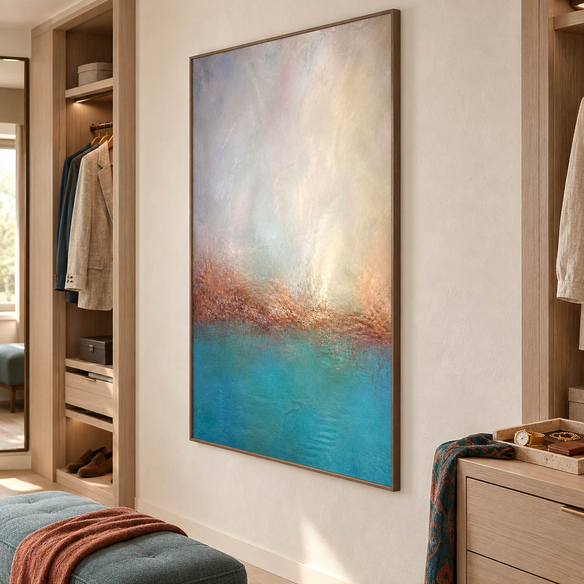 Turquoise coastal painting with a warm shoreline and a luminous pale sky in a brown wood frame in a dressing area.